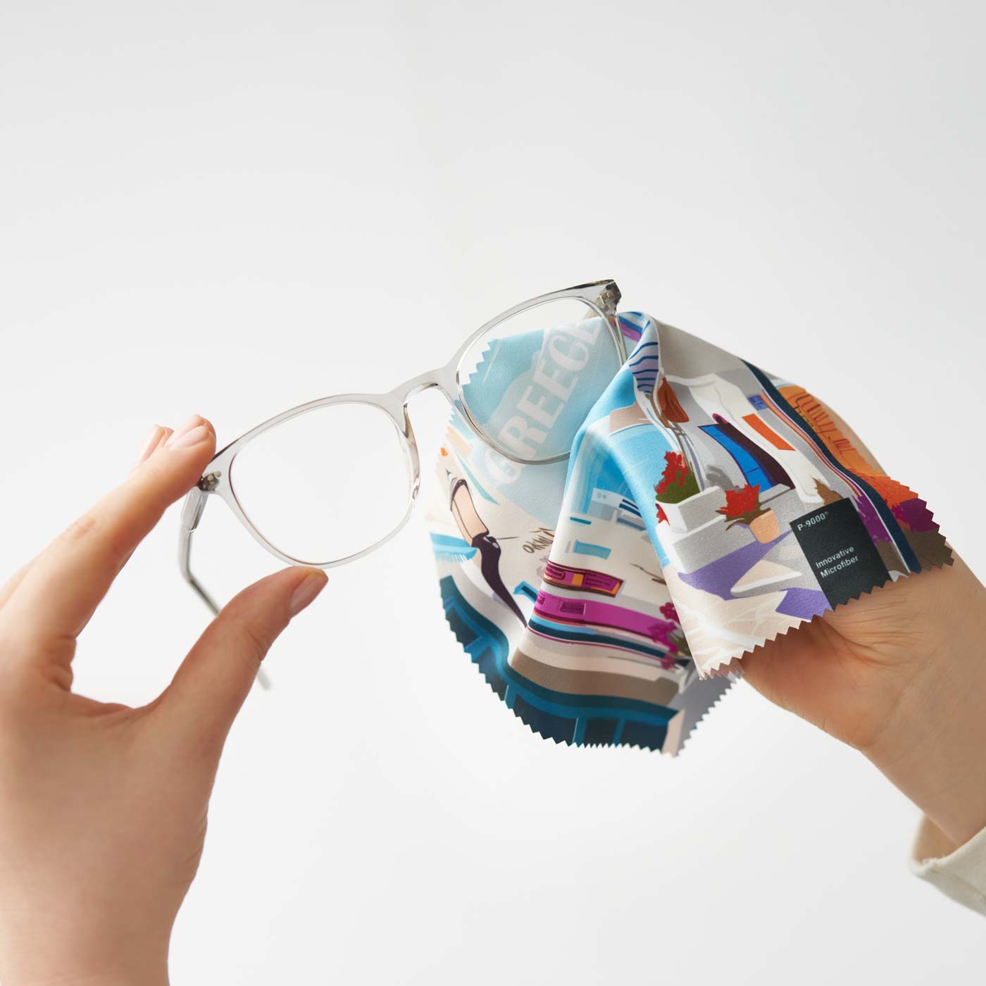 Hände reinigen transparente Brillen mit einem P-9000-Mikrofasertuch mit farbenfrohem Grafikdruck im Griechenland-Stil.